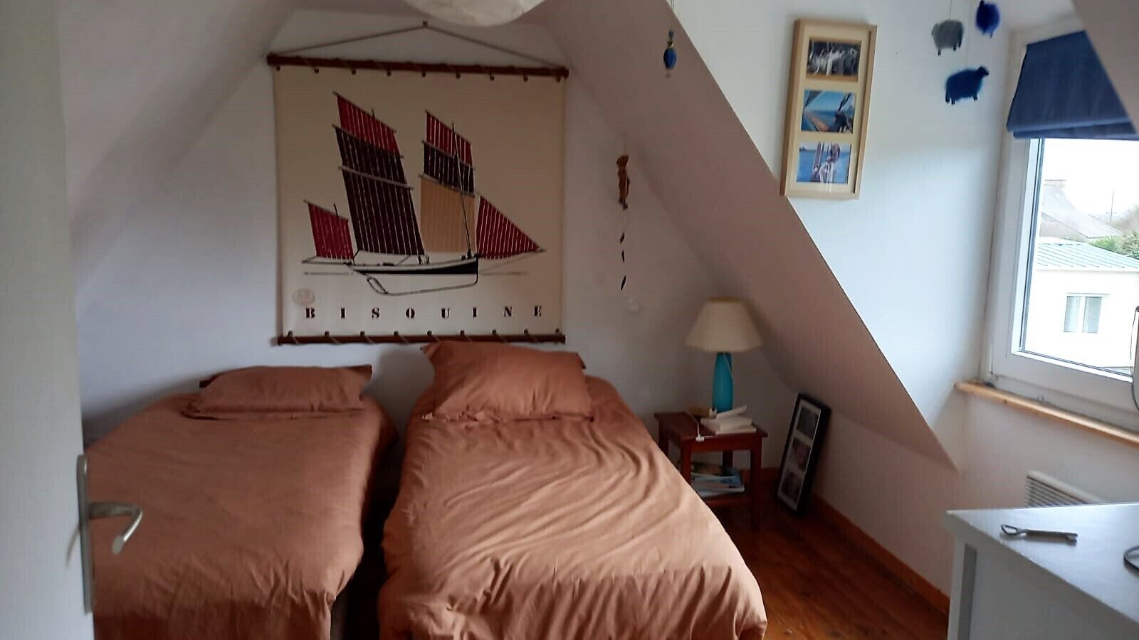 Une chambre avec deux lits, une fenêtre, une lampe et un tableau représentant un voilier accroché au mur.