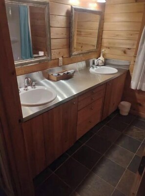Une salle de bain de style rustique, avec des murs en bois, deux lavabos, un miroir et un rideau de douche.