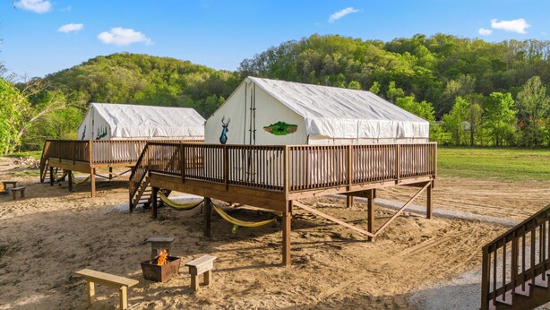 Two wooden decked cabins with white roofs, a fire pit, and a hammock in a sandy outdoor setting. - Furnished Glamping Tent/King Bed/Access to the Red River - Dancing Deer - #6 (Stanton)
