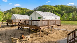Deux cabanes en bois dotées de terrasses et de toits blancs, un foyer et un hamac, le tout installé dans un cadre extérieur sablonneux.