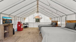 Una habitación con carpa, dos camas, un televisor, un refrigerador rojo y un armario de madera.