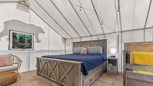 A tented room with a bed, a nightstand, a chair, and a wooden bench.