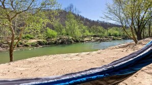 A hammock on a sandy beach with a river and trees in the background.