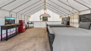 Uma sala com tenda, uma cama, uma escrivaninha, um eletrodoméstico vermelho e um quadro na parede.