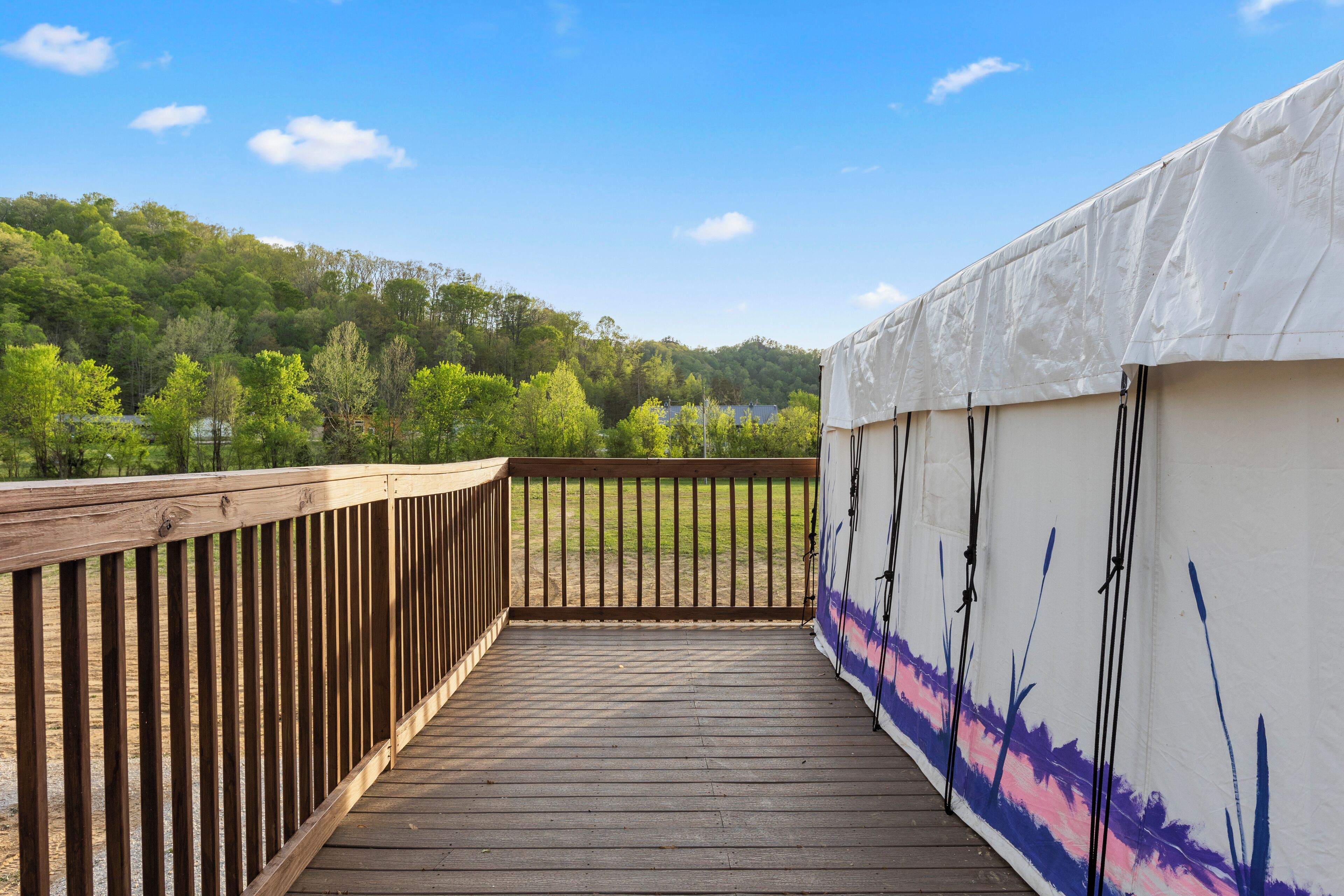 A wooden deck with a view of a forested hill and a tent.