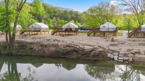 Um camping com iurtes, uma área arenosa, um pequeno corpo d'água e árvores.