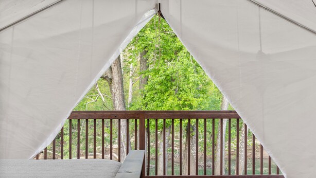 Quarto tipo tenda com deck de madeira e vista para uma floresta.