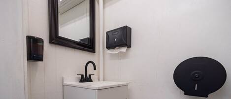 Une petite salle de bain avec un lavabo blanc, un robinet noir, un miroir, un distributeur de savon et des toilettes.