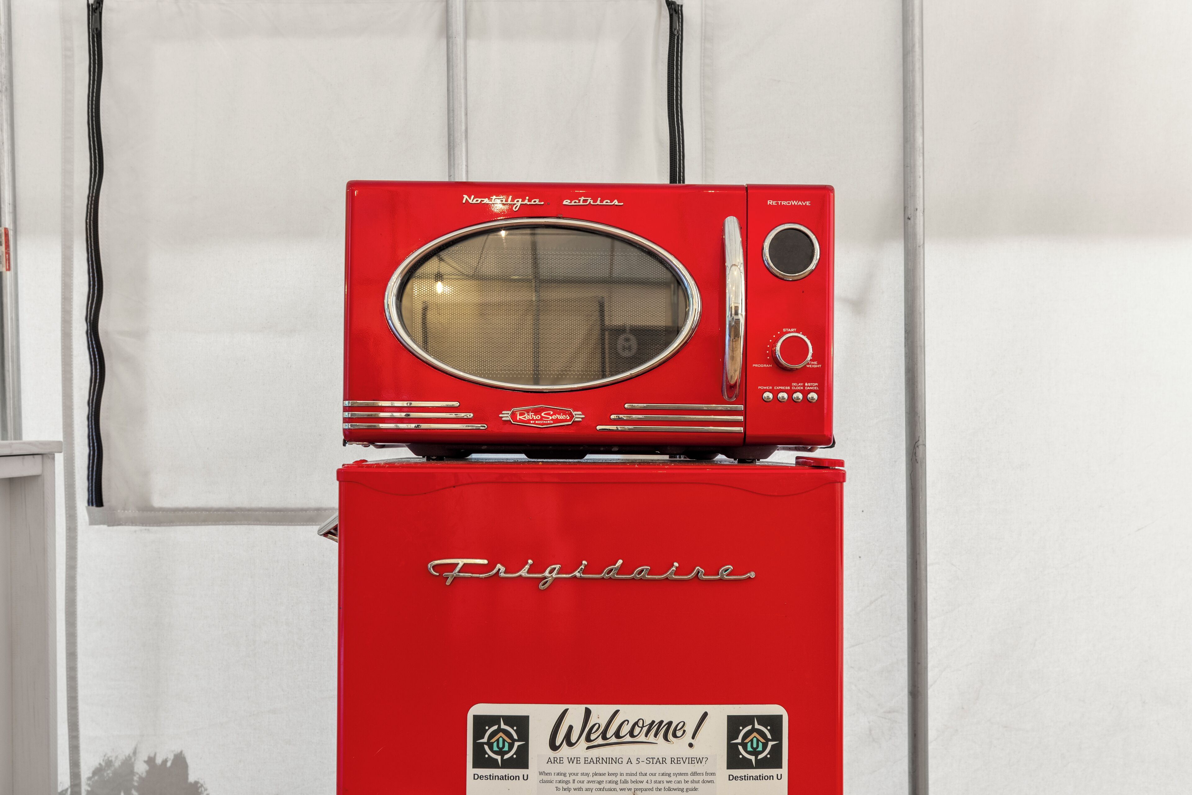 A red Frigidaire refrigerator with a built-in microwave on top, a control panel, and a welcome sign.