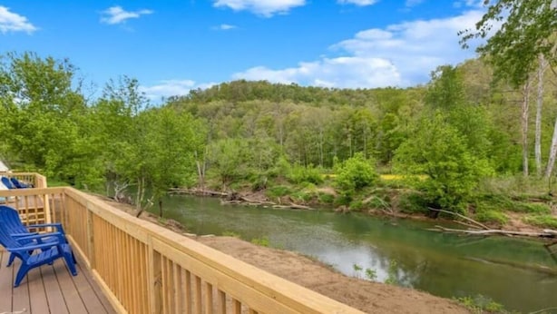 Una terraza de madera con sillas azules que da vista a un río y colinas boscosas.