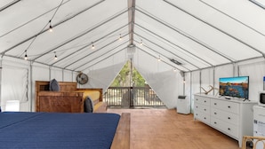 A tented accommodation with a bed, wooden desk, dresser, and a television.