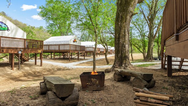 A campsite with wooden cabins, a fire pit, and a dirt path.