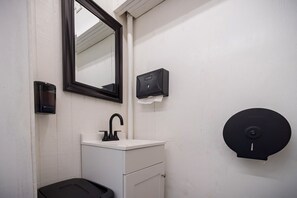 A small bathroom with a white sink, black faucet, a mirror, a soap dispenser, and a toilet.
