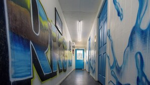 Ein Flur mit Graffiti an den Wänden, einer blauen Tür am Ende und Neonbeleuchtung.