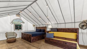 A tented room with a bed, a sofa, a chair, and a fan.