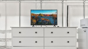 Eine weiße Kommode mit sechs Schubladen und ein flachbildfernseher darüber, der eine herbstliche Landschaft zeigt.