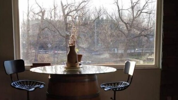 A room with a round table and two chairs, a large wooden barrel labeled 'Franciscan Estate,' and a window with a view of leafless trees. - Creeks Edge offers  full access to charming 8 acres along the river.
 (Canandaigua)