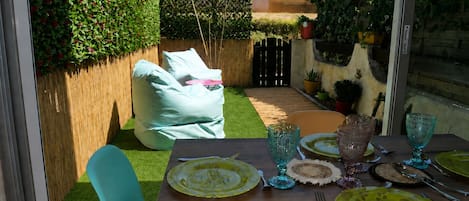 Comedor con una mesa lista para cuatro personas, rodeado por una valla de madera y follaje.