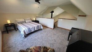 A bedroom with a bed, nightstands, a desk, and a staircase leading to an upper level. - Brightstone Lake Cabin 2 (Rensselaer)