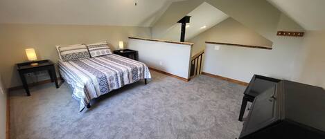 A bedroom with a bed, nightstands, a desk, and a staircase leading to an upper level.