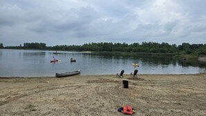 A lakeside setting with canoes, a sandy beach, and chairs. - Brightstone Lake Cabin 2 (Rensselaer)