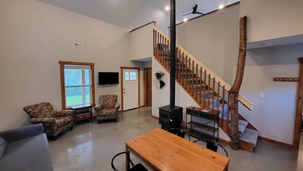 A spacious living room with a wooden staircase, a fireplace, and a television mounted on the wall. - Brightstone Lake Cabin 2 (Rensselaer)