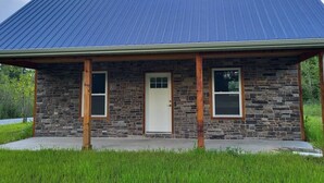 A stone building with a metal roof, a front door, and two windows. - Brightstone Lake Cabin 2 (Rensselaer)