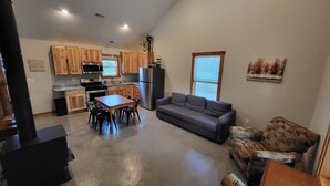 A compact kitchen with wooden cabinets, a refrigerator, and a dining area with a table and chairs. - Brightstone Lake Cabin 2 (Rensselaer)