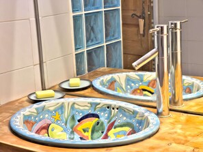 Ein Badezimmer mit Spiegel, zwei Keramiktellern mit Fischmotiven, einer Seifenschale und einem modernen Wasserhahn.