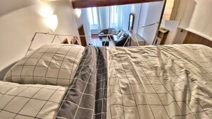 Una cama con colcha y almohadas estampadas, techo de madera y vista a un cuarto con escritorio y silla.