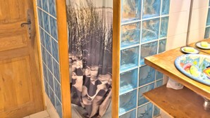 Un baño con cabina de ducha que incluye una puerta de vidrio con un paisaje natural, una puerta de madera y un piso de baldosas.