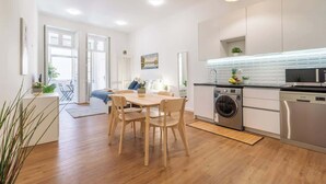 Een moderne keuken met witte kasten, een eethoek met een houten tafel en stoelen, en een wasmachine.