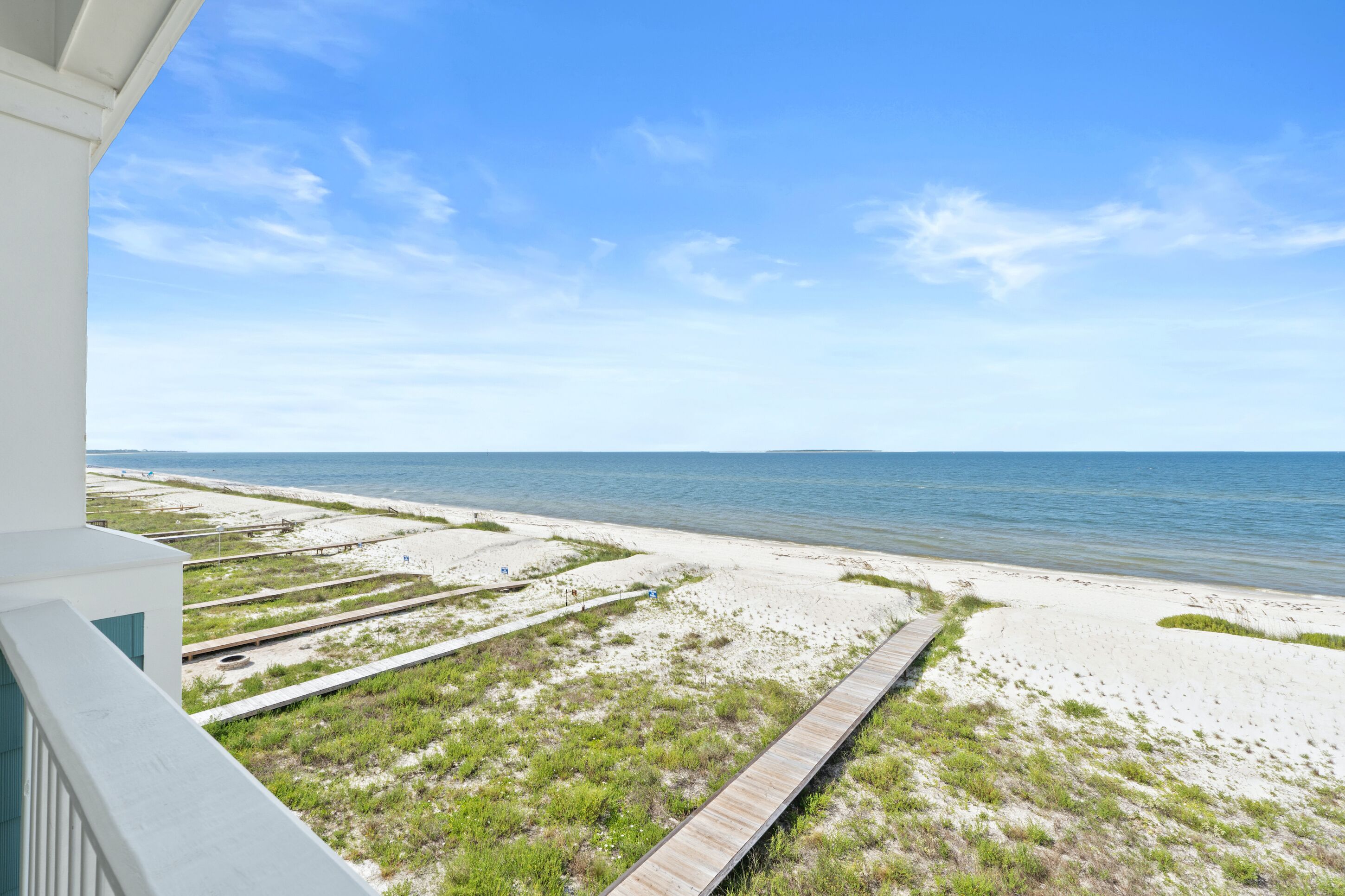 A beach view from a balcony with a wooden boardwalk leading to the shore.