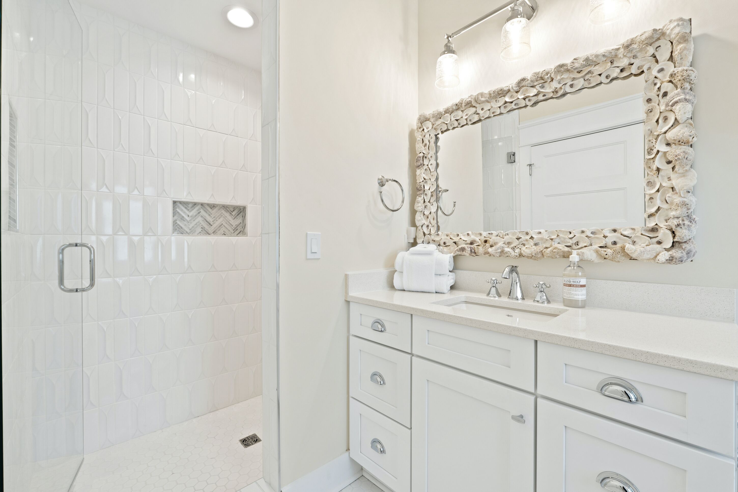 A bathroom with white tiles, a sink with a mirror, and a shower area.