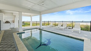 Piscina com vista para a praia, cadeiras de descanso e área de estar coberta.