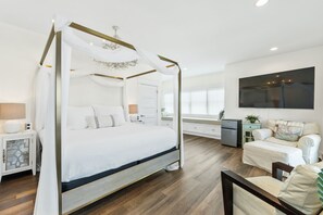 A four-poster canopy bed with a white canopy, a bedside table with a lamp, and a nightstand with a decorative item. - Beach House - Sailfish by PHG (Port St. Joe)