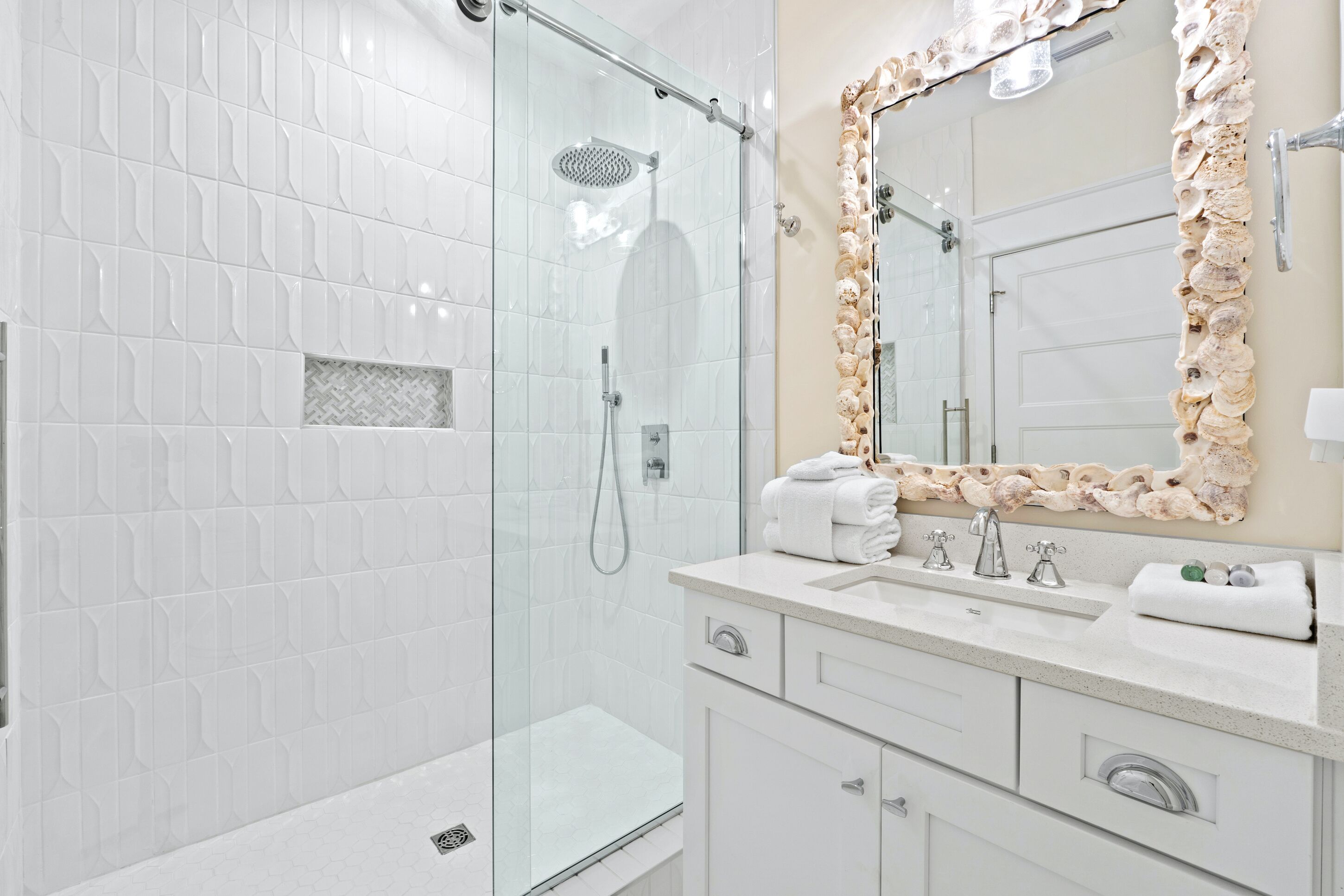 A modern bathroom with a glass-enclosed shower, a large mirror with a decorative frame, and a white vanity with a sink and towel rack.