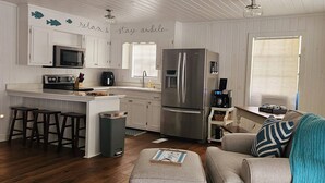 A modern kitchen with white cabinetry, a stainless steel refrigerator, and a built-in oven. There are wooden stools and a small island with a sink. - Lakeside Chalet on Beautiful Gantt Lake! (Dozier)