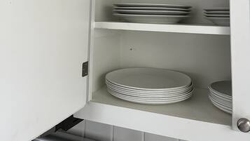 A kitchen cabinet with shelves containing plastic containers and stacked plates.