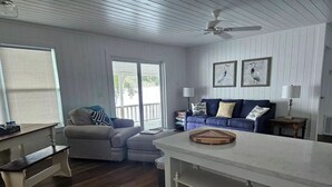 A living room with a sofa, a coffee table, a bench, and a dining area with a white table and shelves. - Lakeside Chalet on Beautiful Gantt Lake! (Dozier)