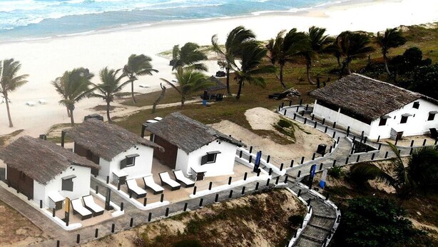 Une propriété située en bord de mer, avec des bungalows aux toits de chaume, une plage de sable et des palmiers.