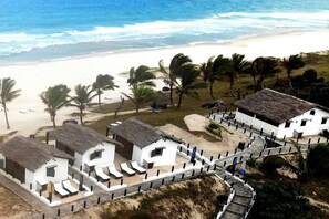 Une propriété située en bord de mer, avec des bungalows aux toits de chaume, une plage de sable et des palmiers.