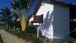 Un bâtiment situé au bord de la plage, doté d’un toit de chaume, entouré de palmiers et bordé d’un sentier sablonneux.