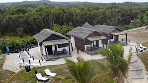 Un complexe hôtelier doté de bungalows aux toits de chaume, d’un espace de restauration en plein air et offrant une vue sur une colline boisée.