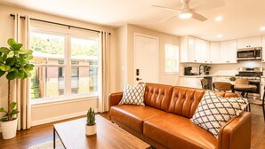 A living room with a brown leather sofa, a coffee table, and a potted plant. - (12) Book Now & Save 10%! Modern July Apartment (Houston)