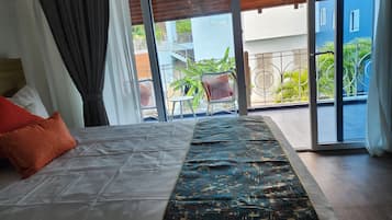 A bedroom with a bed, a view of the outside balcony, and a window with curtains.