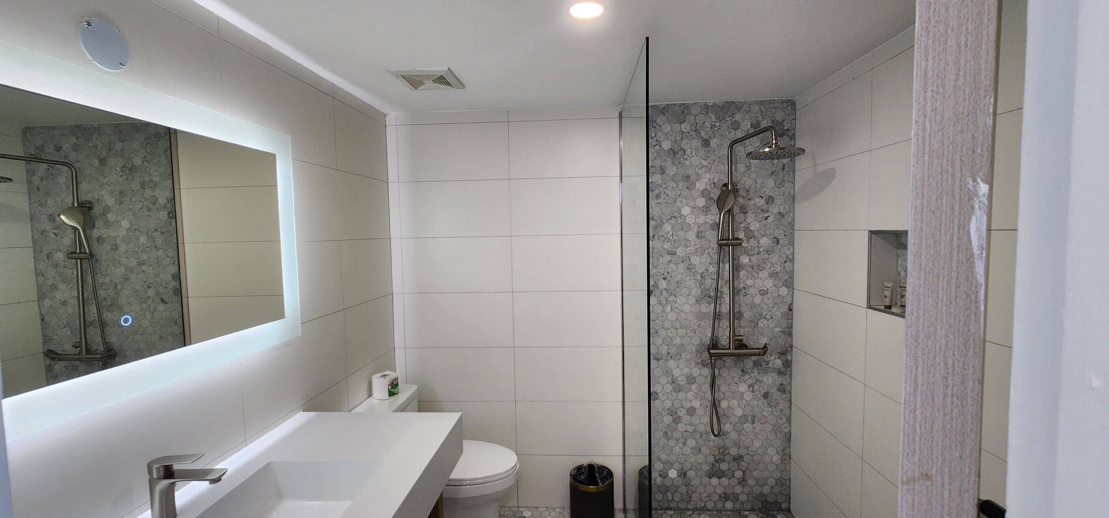 A modern bathroom with a white sink, toilet, and shower area with a glass door.