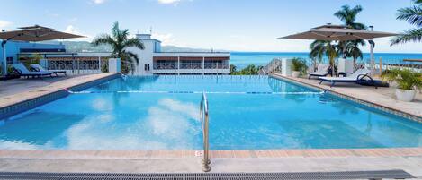 A swimming pool with a view of the ocean, lounge chairs, and umbrellas.
