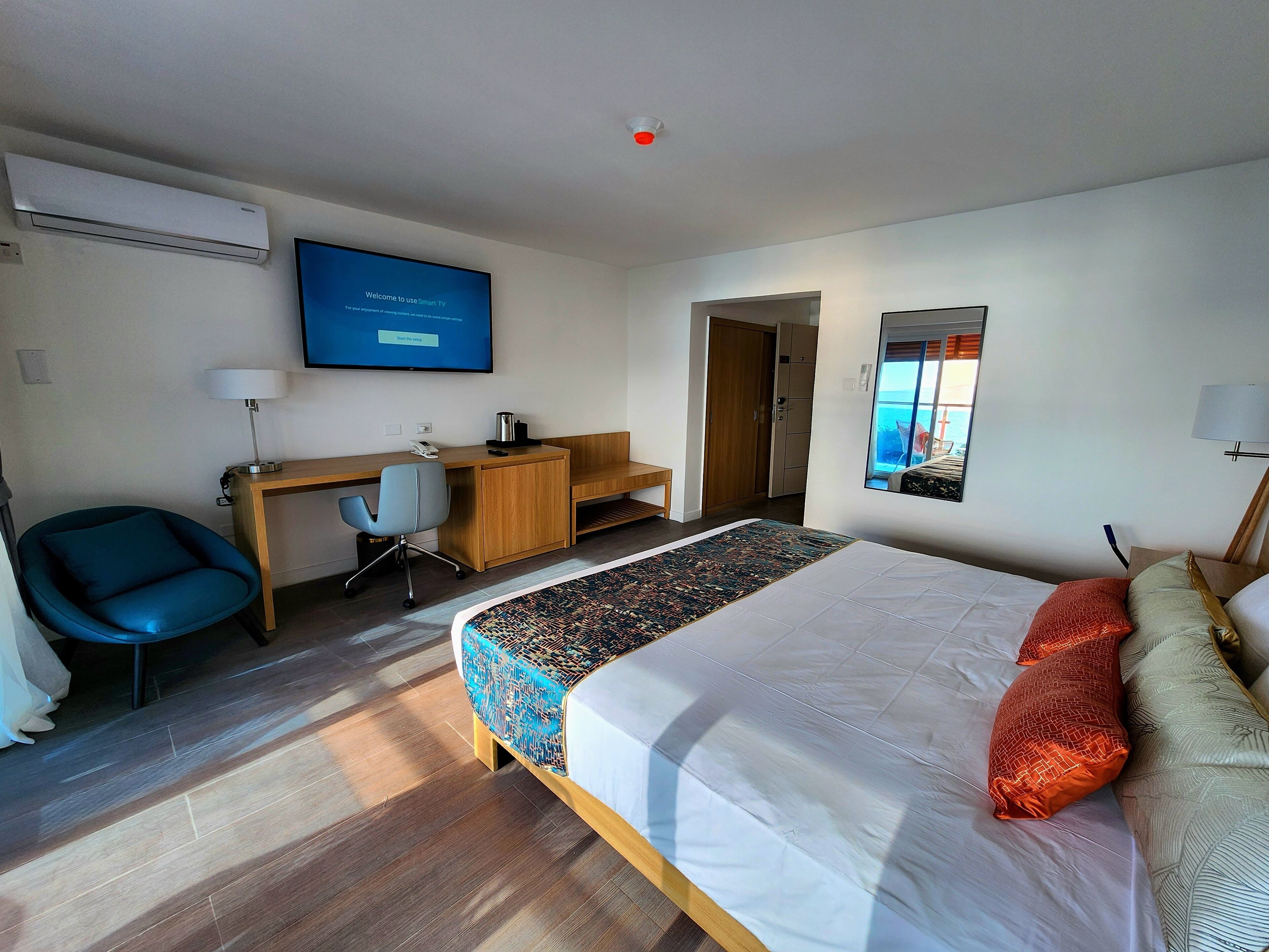 Habitación de hotel con cama, escritorio, silla, televisor y puerta que da a otra habitación.