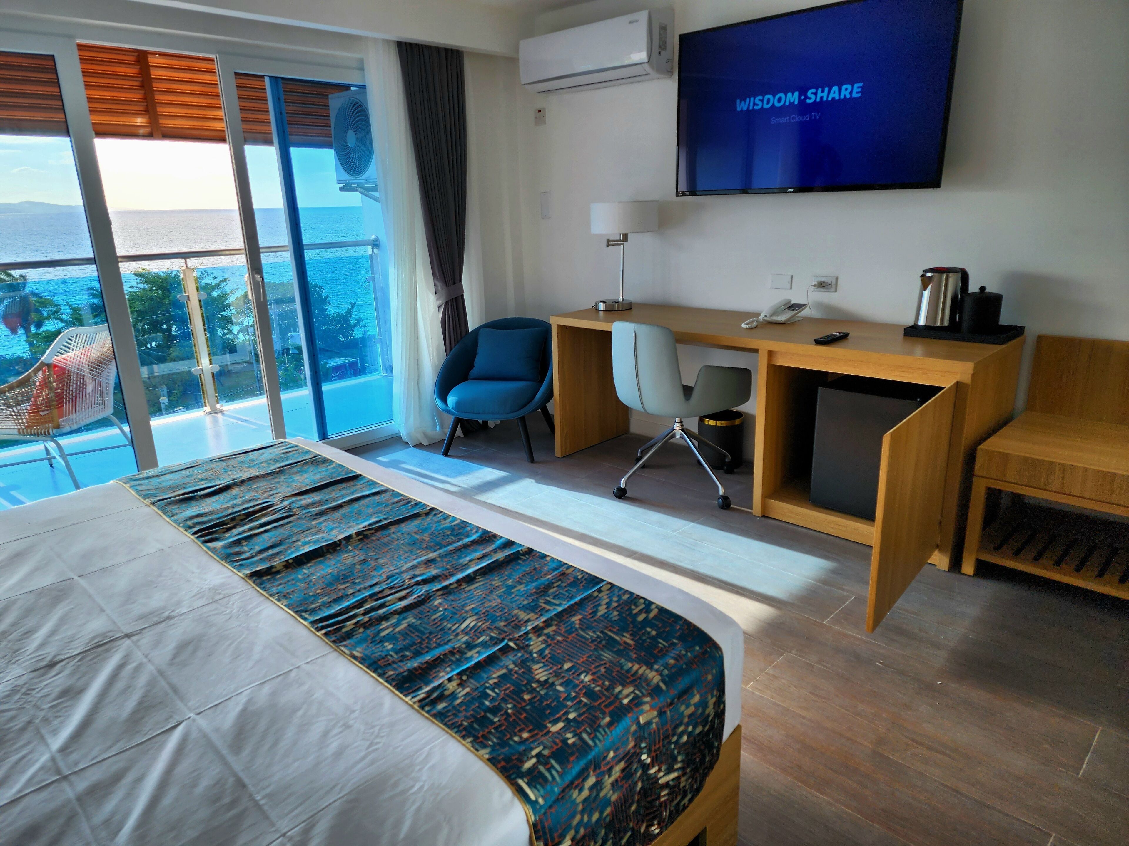 Ein Hotelzimmer mit Bett, Schreibtisch, Stuhl, Fernseher und einem Balkon mit Meerblick.
